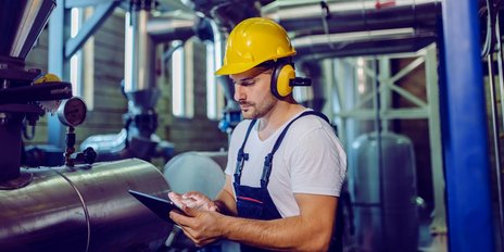 Ein Mann mit Bauhelm steht mit einem Tablet in einem Rohrraum